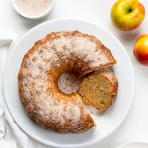 Apple Cider Donut Bundt Cake on a white platter with a couple of pieces removed but one left and leaning against the cake.