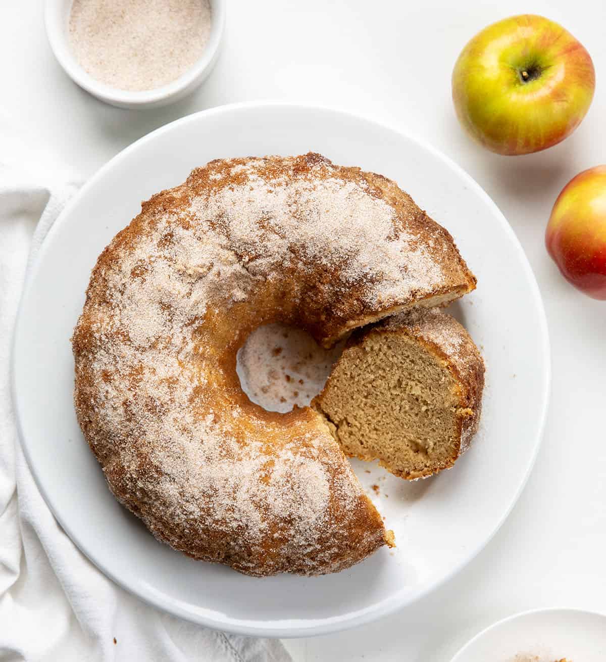 Apple Cider Donut Bundt Cake on a white platter with a couple of pieces removed but one left and leaning against the cake.