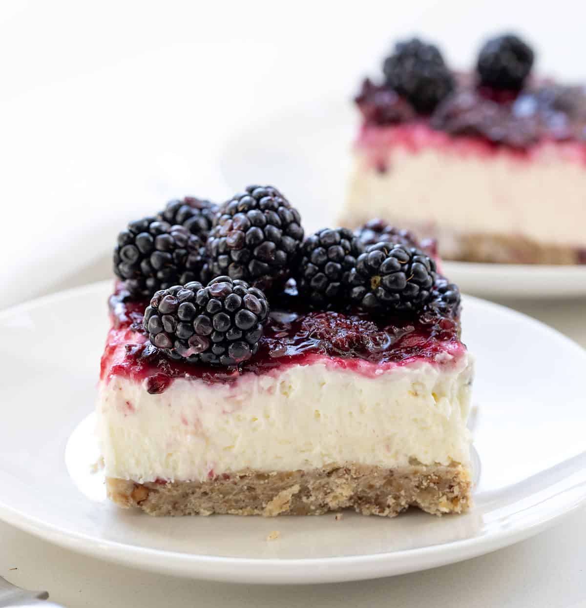White plates with Blackberry Cream Cheese Bars on them on a white table.