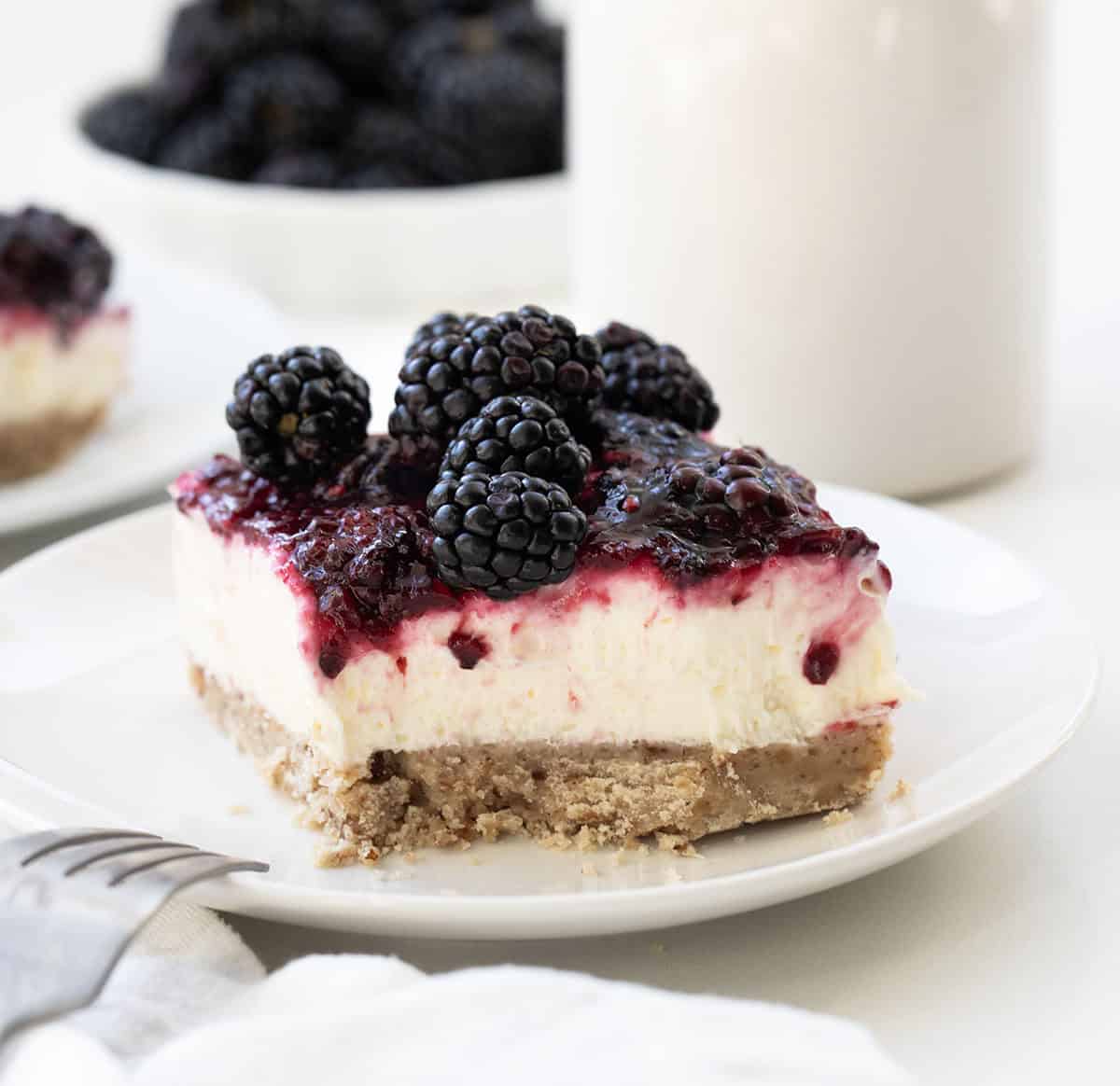 White plate with Blackberry Cream Cheese Bar on it with a bite removed and fork resting on the plate.