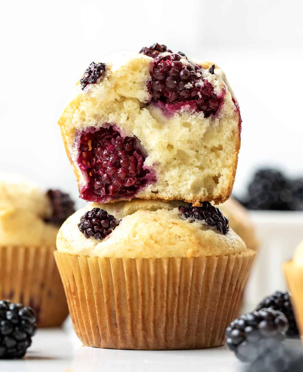 Blackberry Muffins stacked with the top muffin halved showing inside texture.