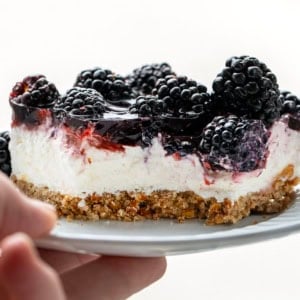 Hand holding a white plate with Blackberry Pretzel Salad with a bite removed.