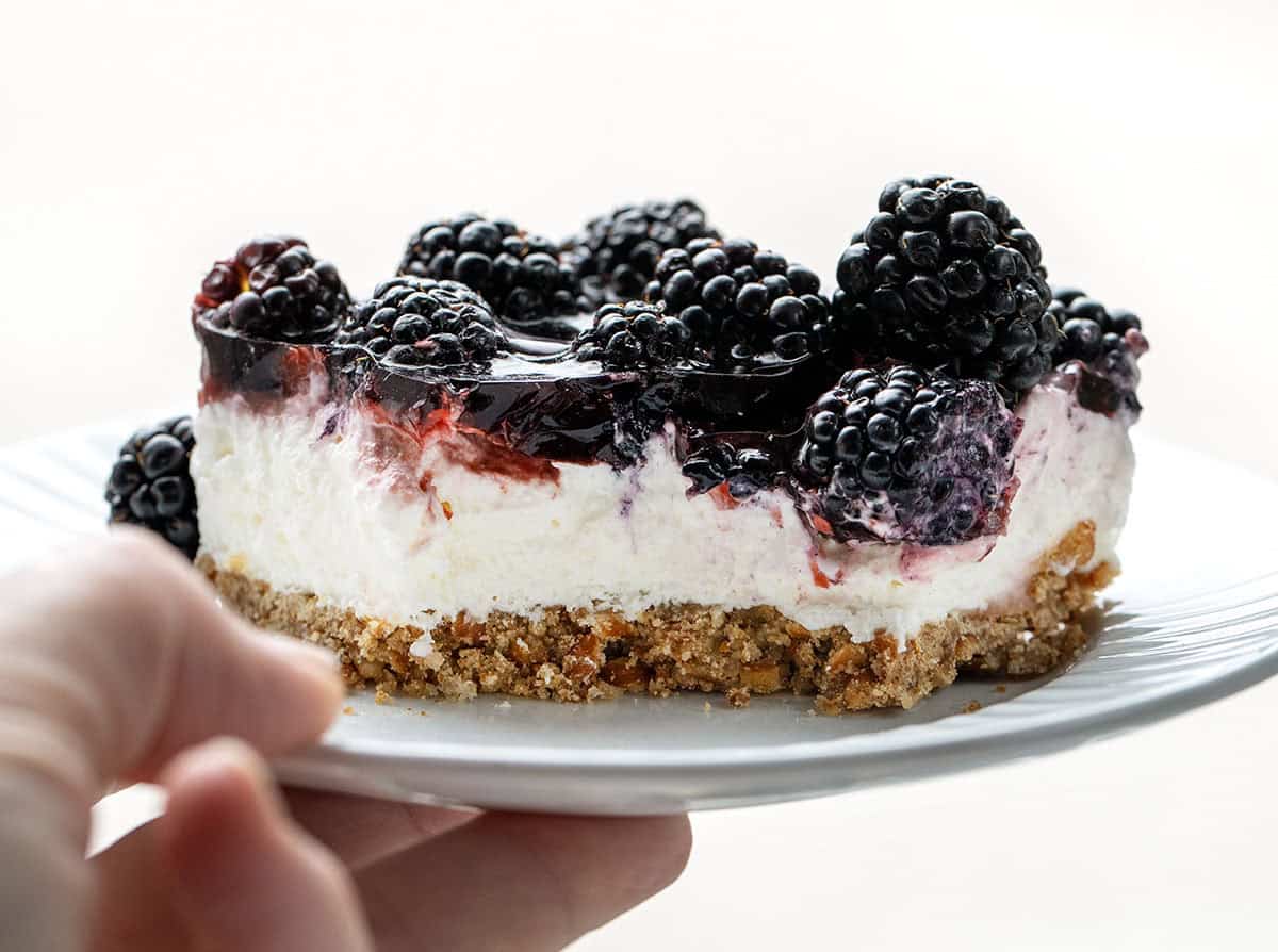 Hand holding a white plate with Blackberry Pretzel Salad with a bite removed.