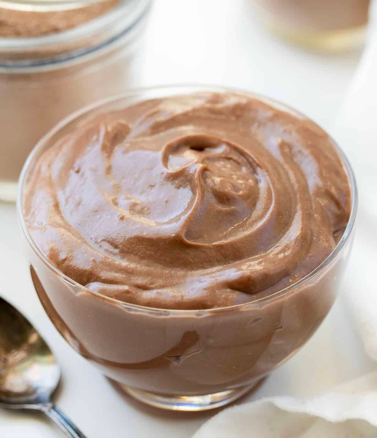 Bowl of homemade cooked chocolate pudding next to a jar of chocolate pudding mix.