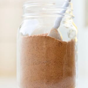 Jar of Chocolate Pudding Mix on a white counter with a spoon in the jar.