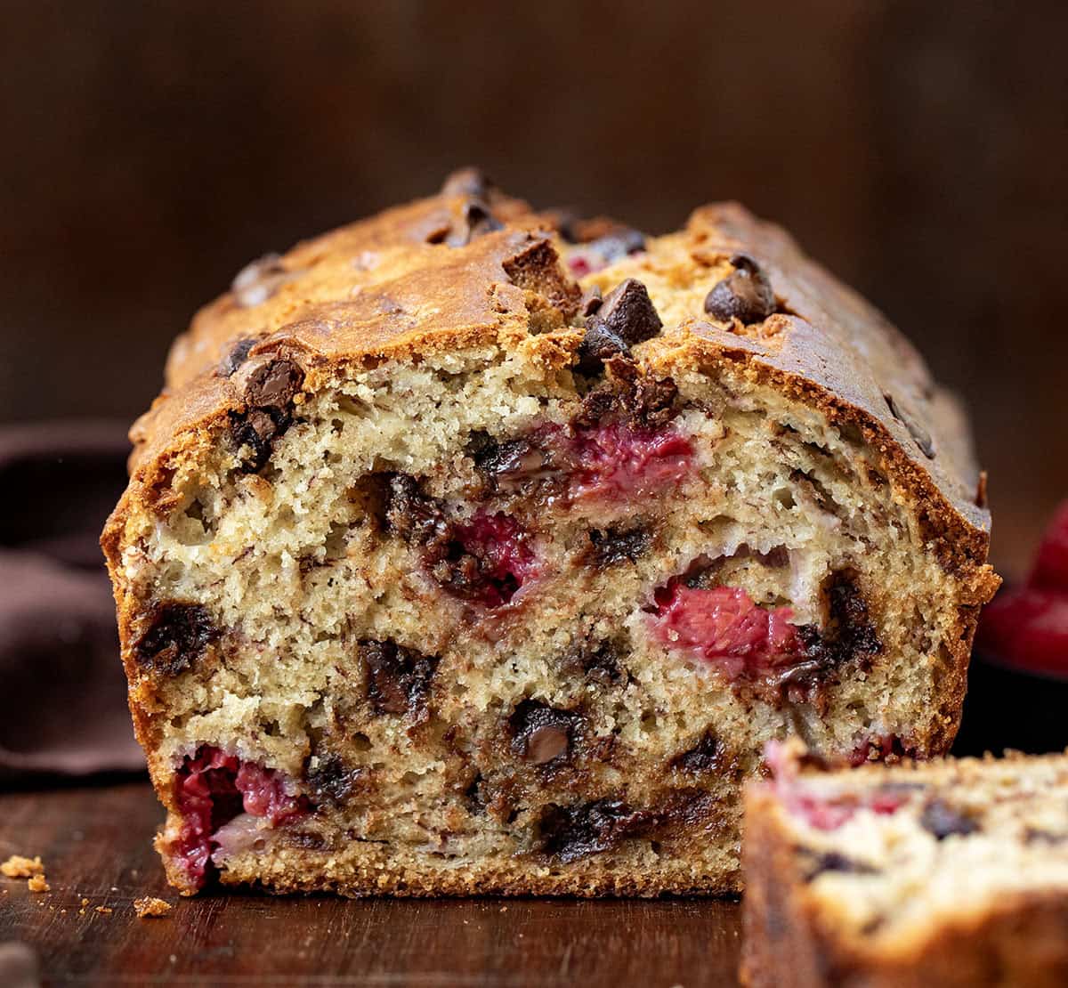 This chocolate raspberry banana bread is soft, moist, and packed with melty chocolate chips and juicy raspberries in every bite. Loaf of Chocolate Raspberry Banana Bread that has been cut into showing the texture inside on a wooden table.