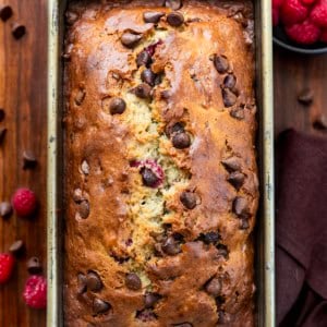 Loaf of Chocolate Raspberry Banana Bread surrounded by raspberries and chocolate from overhead.