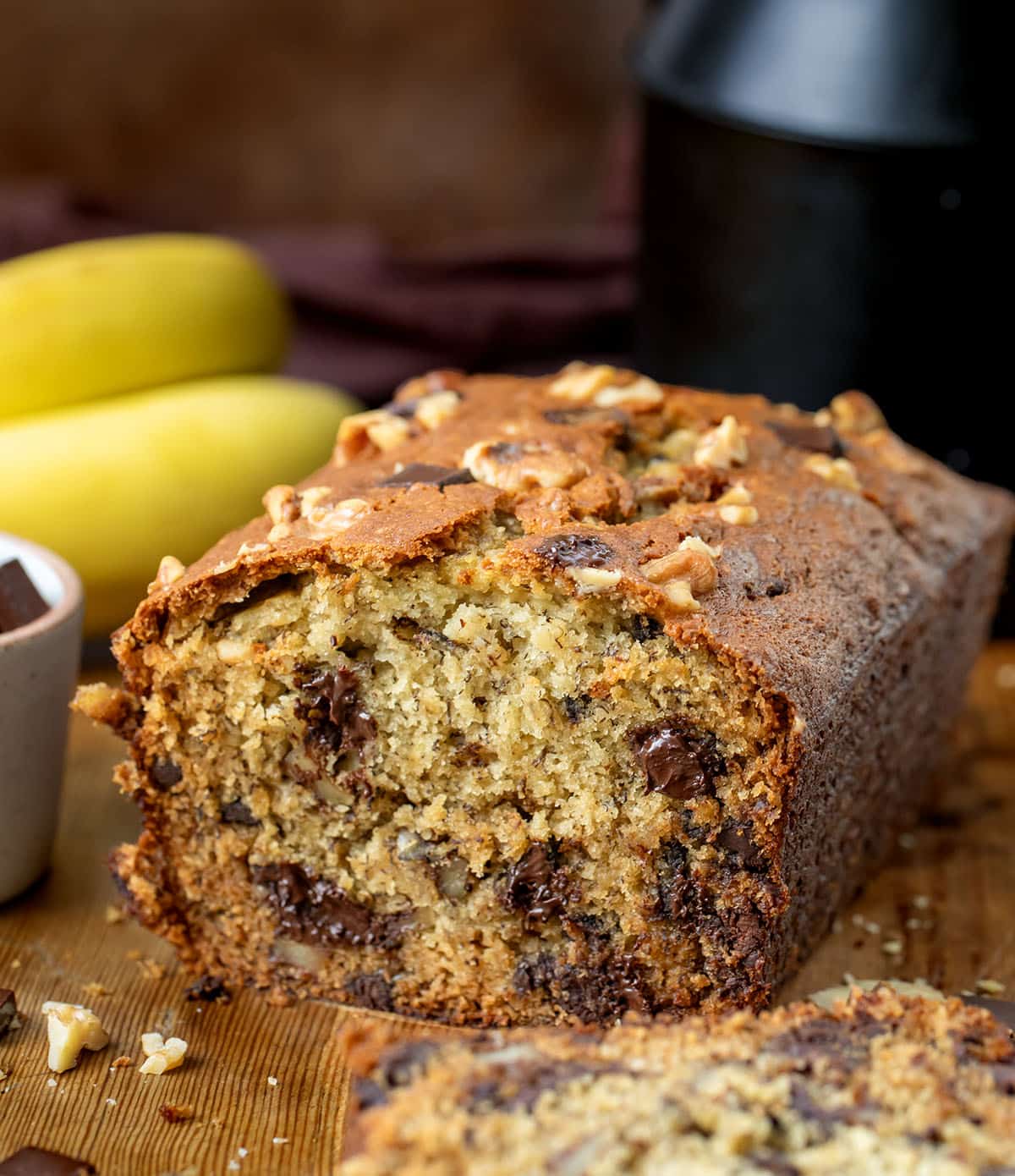 Loaf of Chunky Monkey Banana Bread that has been cut showing the inside texture on a wooden table.