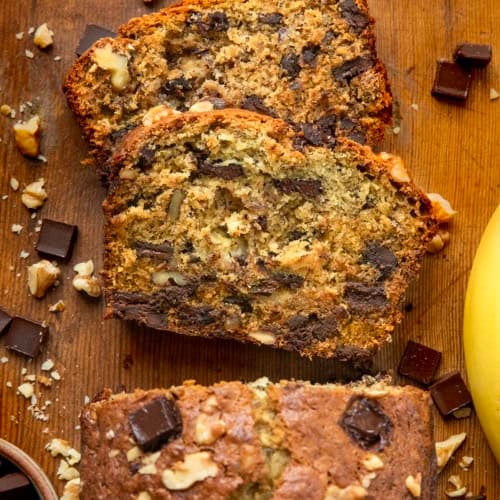 Looking down on pieces of Chunky Monkey Banana Bread laying flat near the loaf on a wooden table.