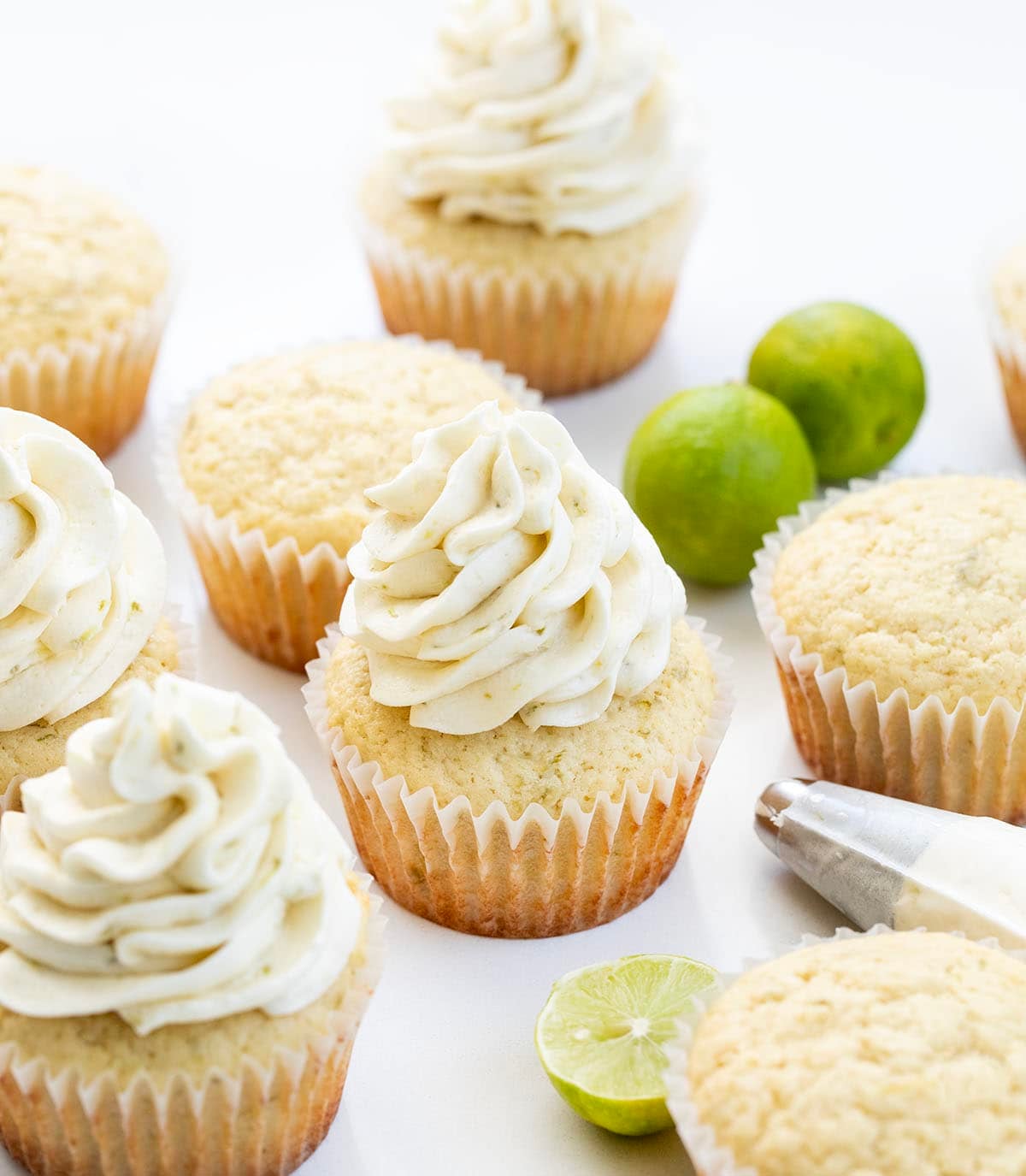 Key Lime Cupcakes with Key Lime Ermine piped on it with a piping bag next to the cupcakes.