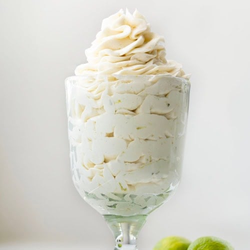 Glass with Key Lime Ermine Frosting piped into it on a white table.