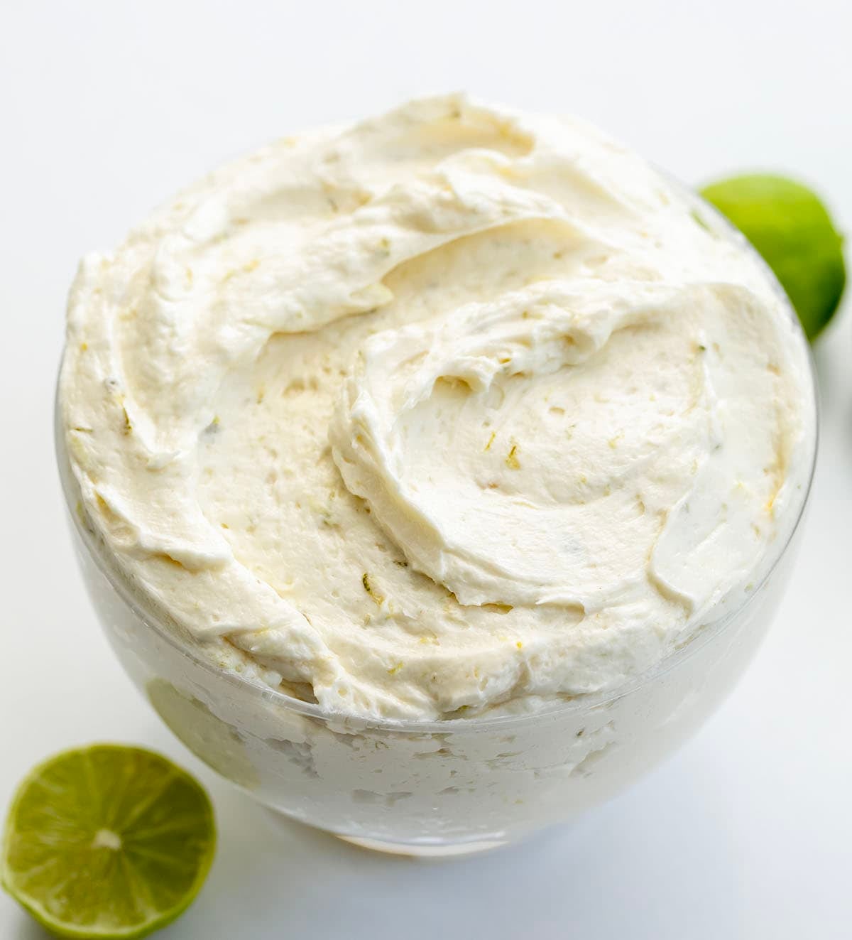 This Key Lime Ermine Frosting is light, silky, and full of bright citrus flavor from fresh key lime juice and zest. It whips up into a smooth, cloud-like frosting thatโs less sweet than traditional buttercream but still rich enough to pipe or spread beautifully! Bowl of Key Lime Ermine Frosting on a white table with fresh key limes.