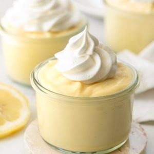 Jars of Lemon Pudding with whipped cream on a white table with fresh lemon.