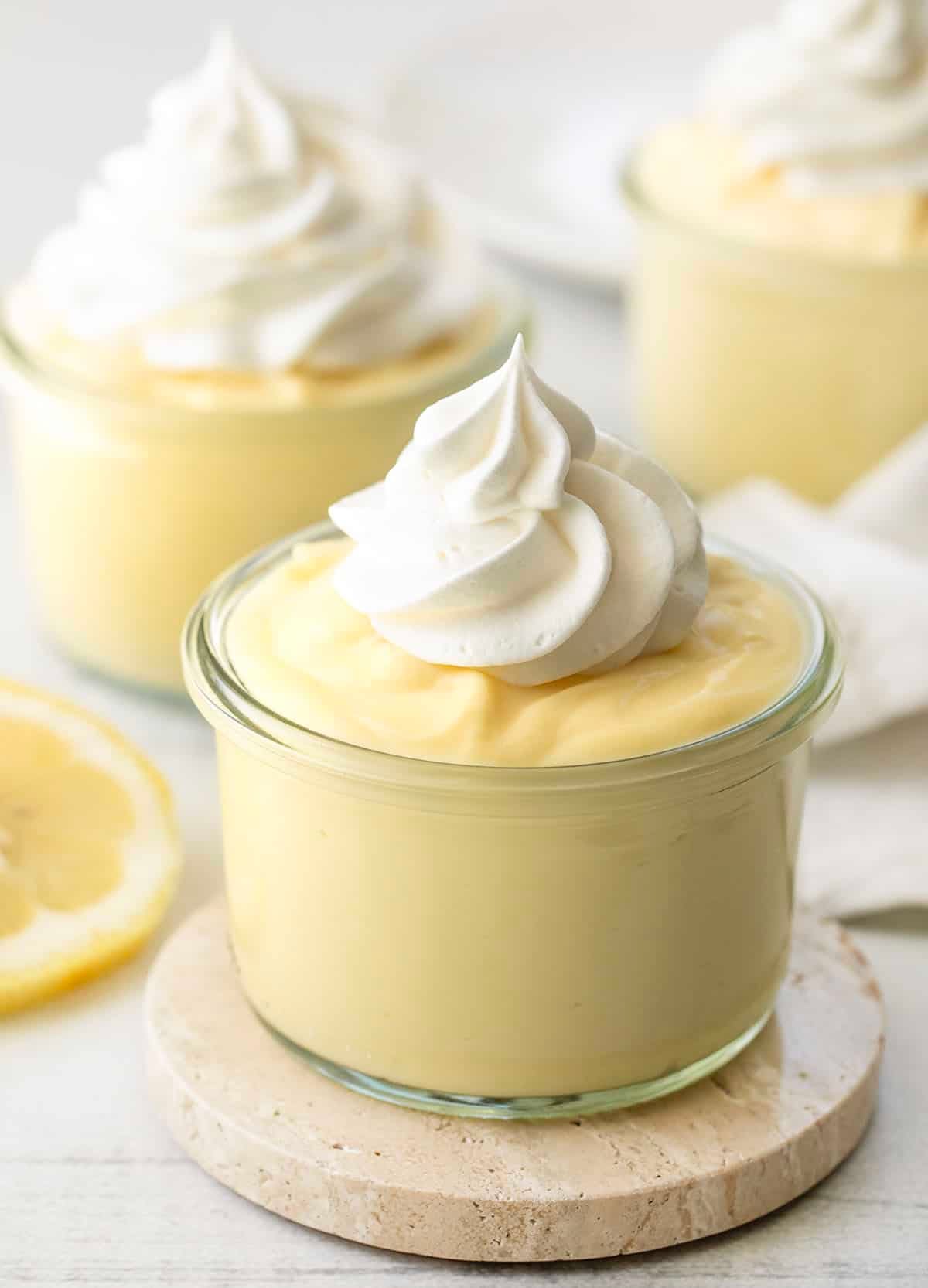 Jars of Lemon Pudding with whipped cream on a white table with fresh lemon.