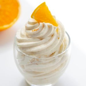 Piped Orange Ermine Frosting in a small glass with fresh orange.