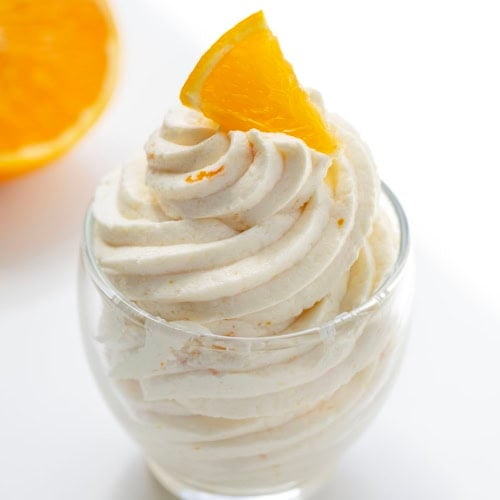 Piped Orange Ermine Frosting in a small glass with fresh orange.
