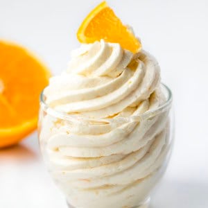 Piped Orange Ermine Frosting in a small glass with fresh orange.