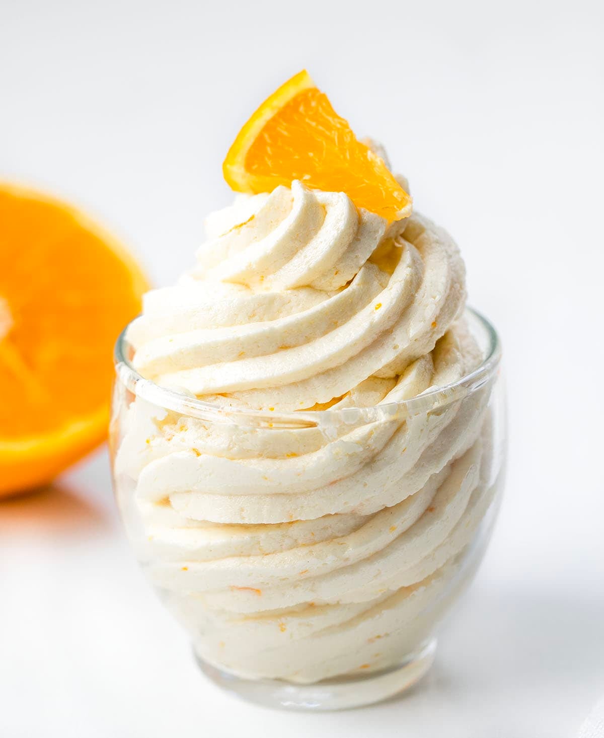 Piped Orange Ermine Frosting in a small glass with fresh orange.