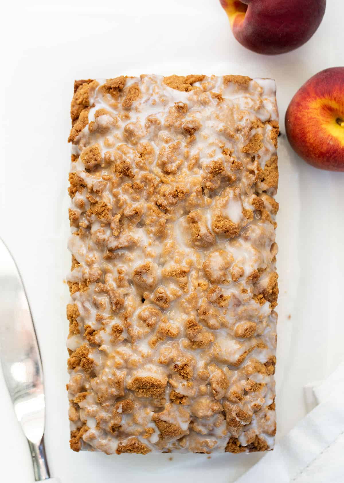 This Peach Cobbler Bread is an easy quick bread that tastes just like peach cobbler in loaf form. It’s soft and tender with juicy peaches in every bite, plus a buttery cinnamon crumble baked right on top! Loaf of Peach Cobbler Bread on a white table from overhead.