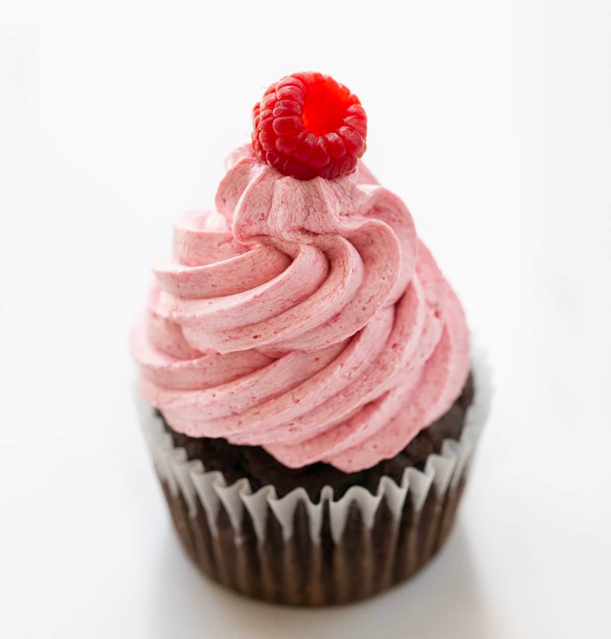 Raspberry Ermine Frosting piped onto a chocolate cupcake with a fresh raspberry on top.
