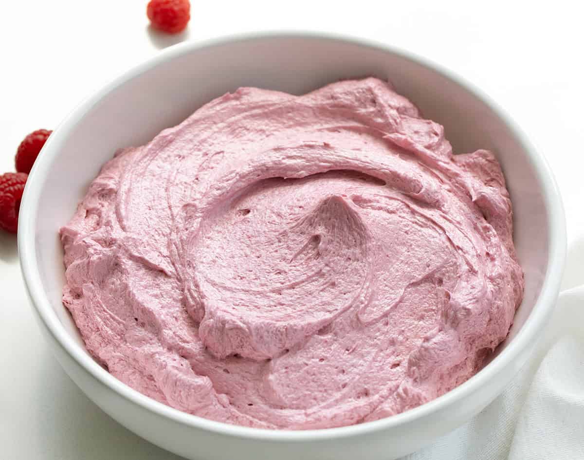 White bowl filled with Raspberry Ermine Frosting on a white table with a few fresh raspberries.