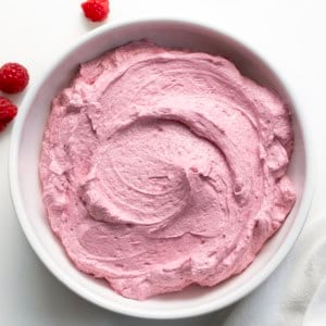 White bowl filled with Raspberry Ermine Frosting on a white table with a few fresh raspberries.