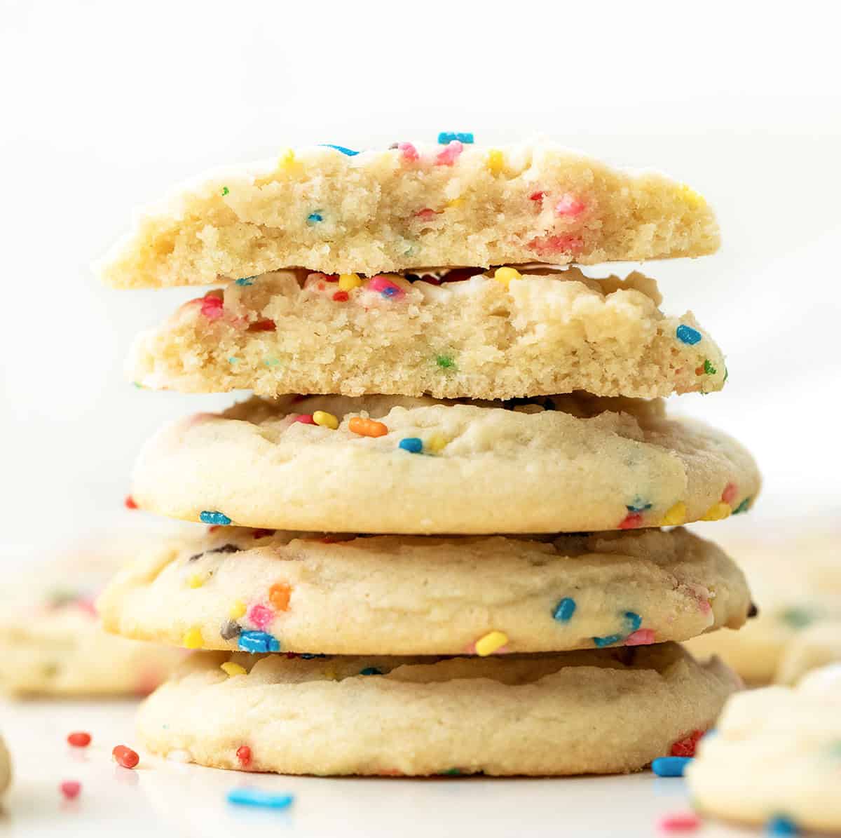 Stack of Sprinkles Sugar Cookies with the top cookie broken in half showing inside texture.