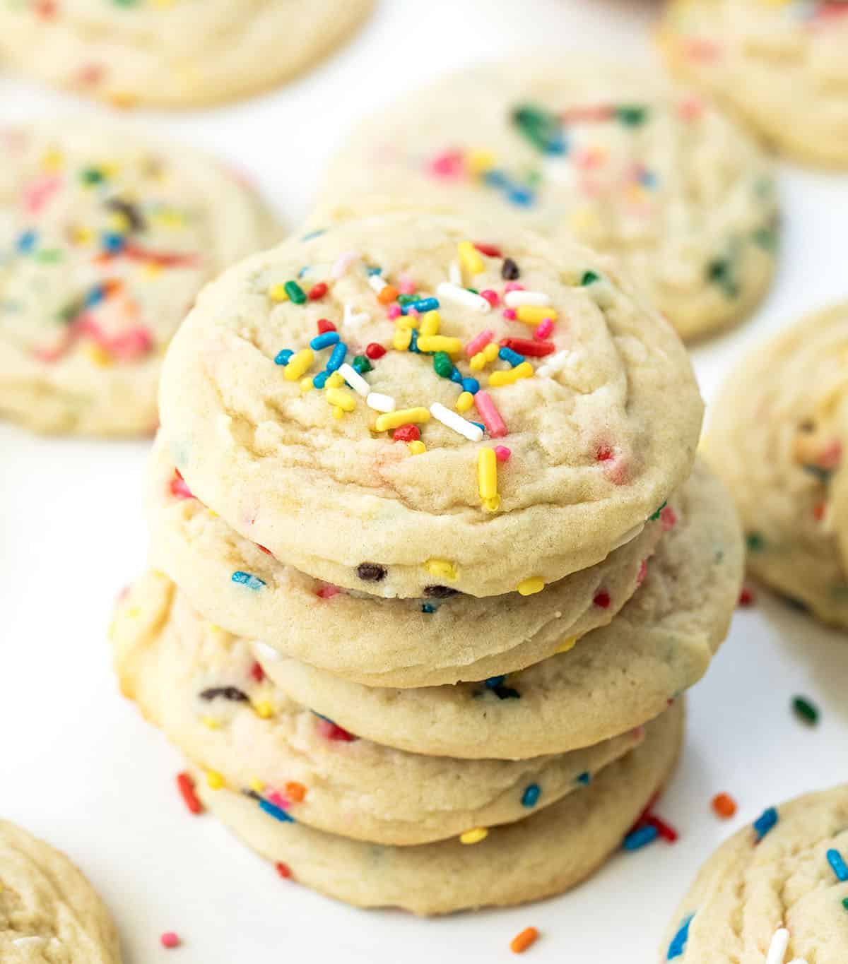 Stack of Sprinkles Sugar Cookies on a white table surrounded by more cookies.