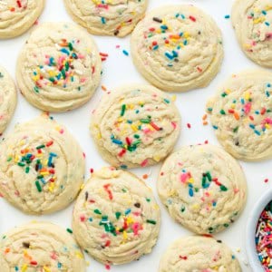 Sprinkles Sugar Cookies on a white table from overhead with a bowl of rainbow sprinkles nearby.