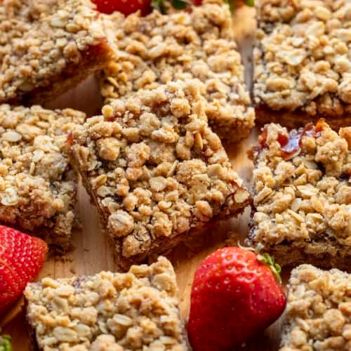 Strawberry Oatmeal Crumble Bars cut up and stacked on each other next to fresh strawberries.
