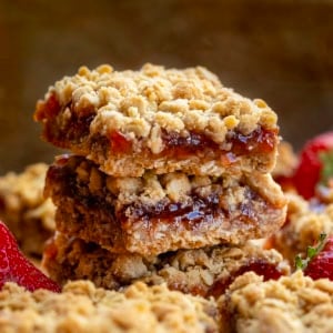 Stack of Strawberry Oatmeal Crumble Bars on a wooden table with fresh strawberries.
