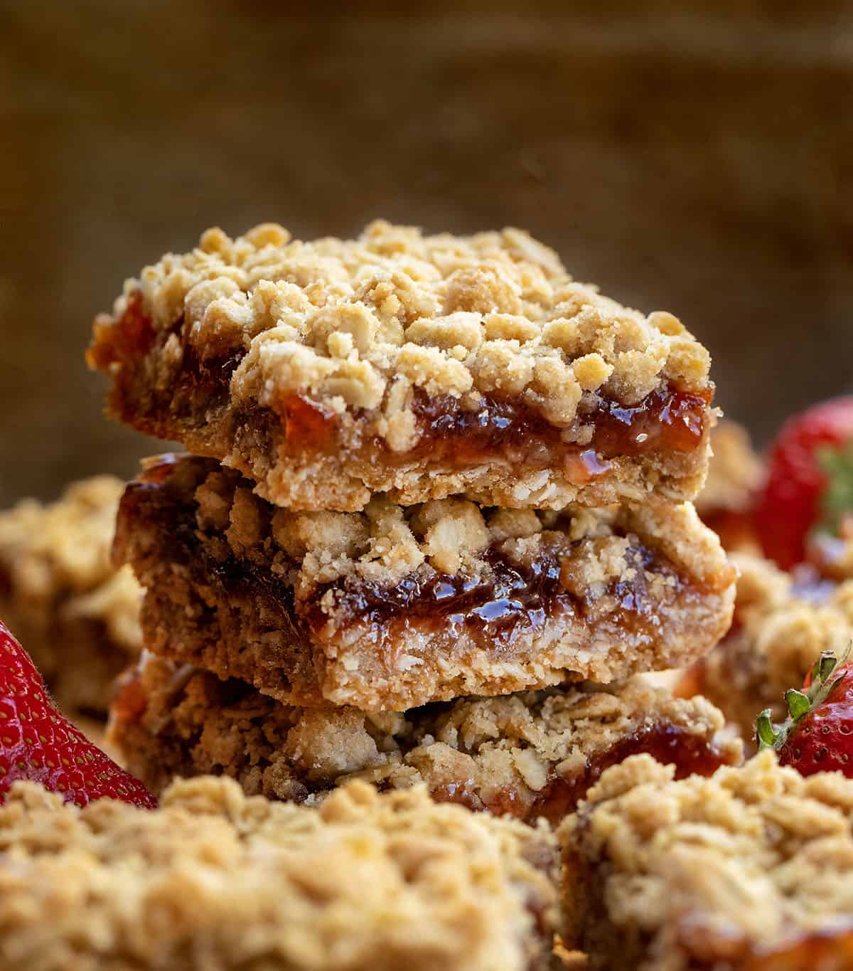 Stack of Strawberry Oatmeal Crumble Bars on a wooden table with fresh strawberries.