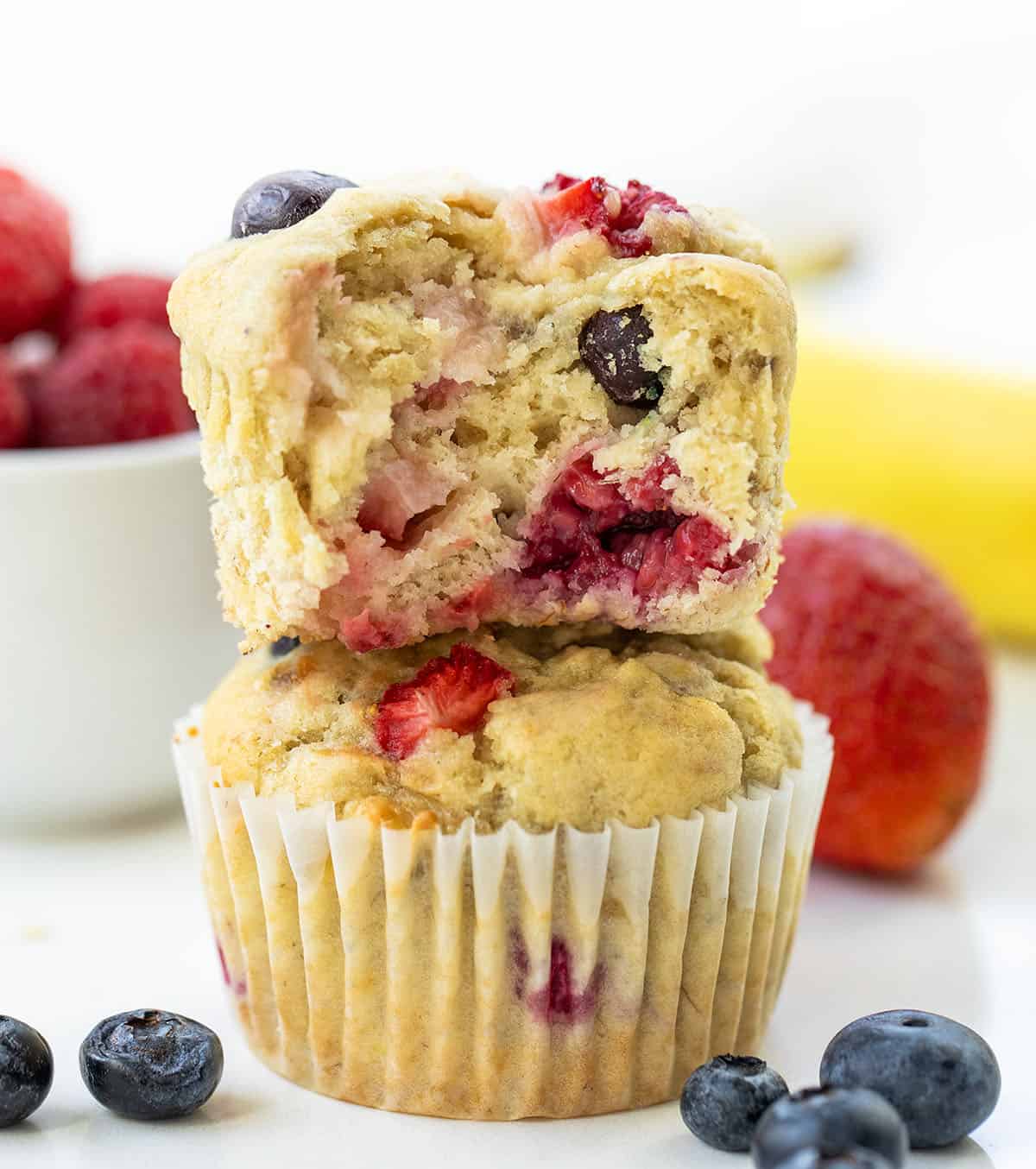 Stack of Triple Berry Banana Muffins with the top muffin halved showing tender inside.