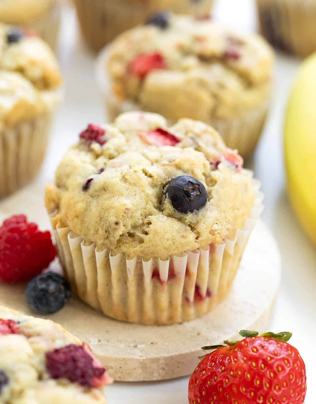 Close up of Triple Berry Banana Muffins with fresh strawberry, raspberry, blueberry, and banana.