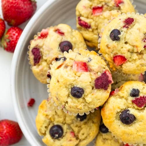 Looking down on Triple Berry Banana Muffins in a bowl on a white table.