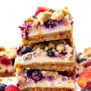 Stack of Triple Berry Cheesecake Bars on a white table.