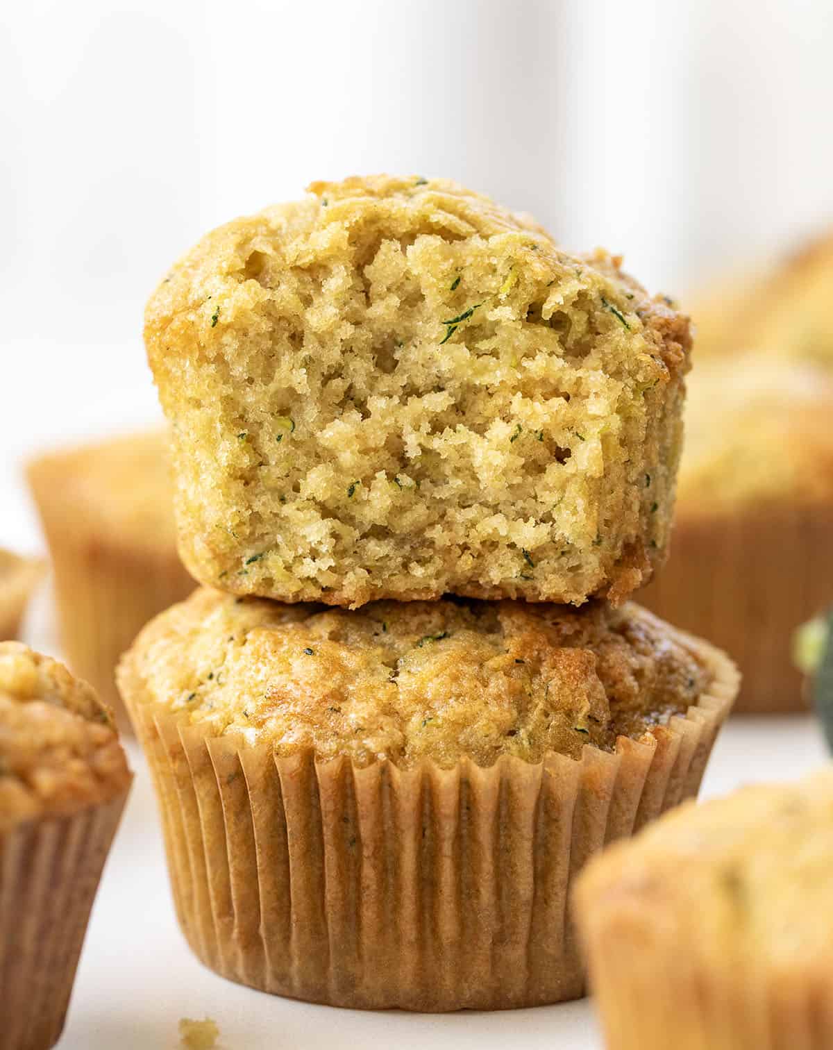 Zucchini Muffins stacked and the top muffin is halved showing inside texture.