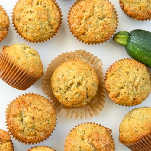Zucchini Muffins on a white table with a zucchini from overhead.