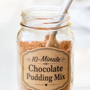 Jar of Chocolate Pudding Mix on a white counter with a spoon in the jar.