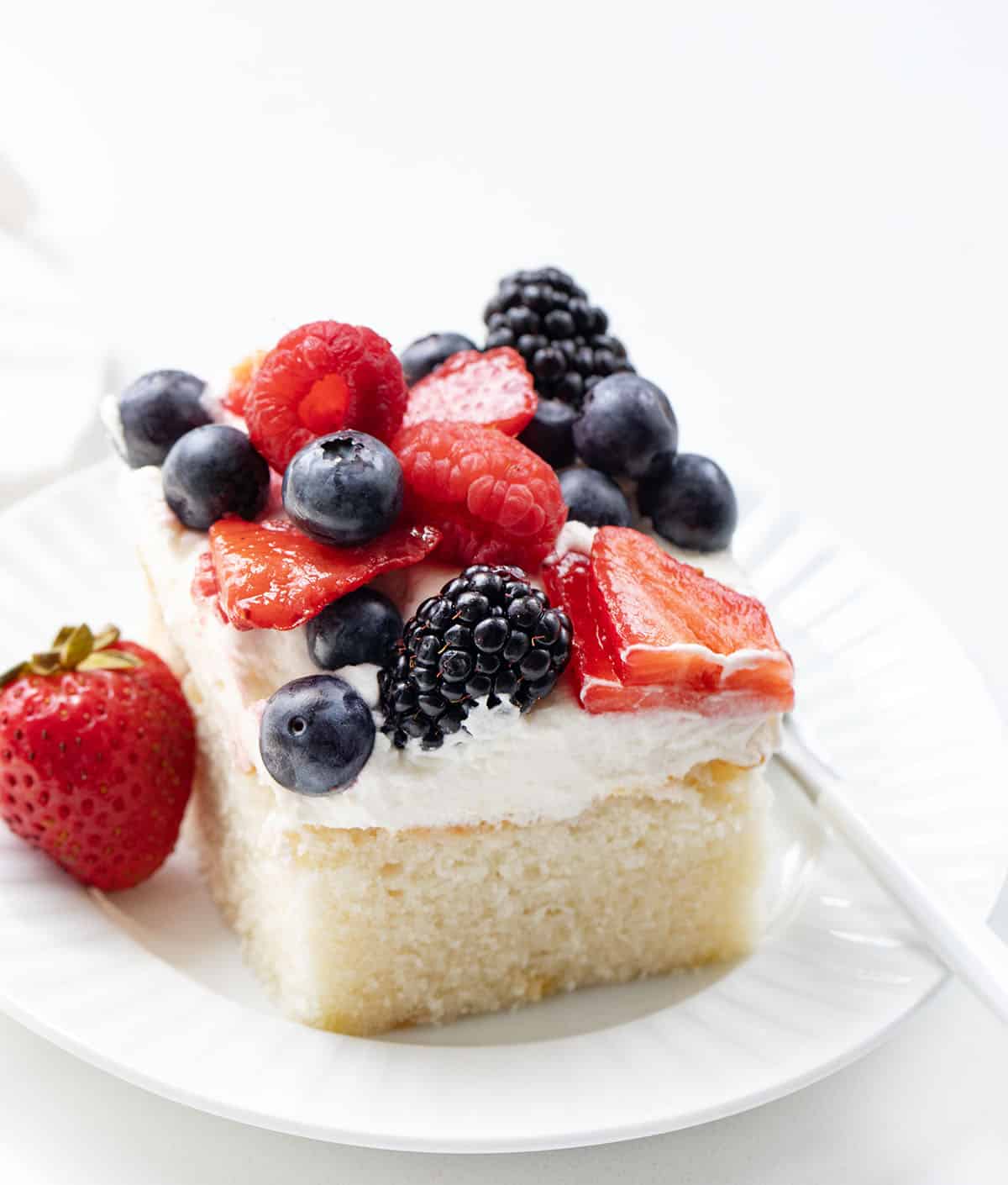 Slice of Berries & Cream Sheet Cake on a white plate on a white counter.