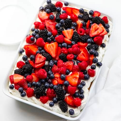 Berries & Cream Sheet Cake on a white table with white plates and a white hand towel next to the cake pan.