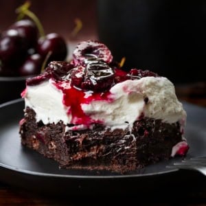 Close up of a Black Forest Brownie with a bite removed on a plate on a wooden table.