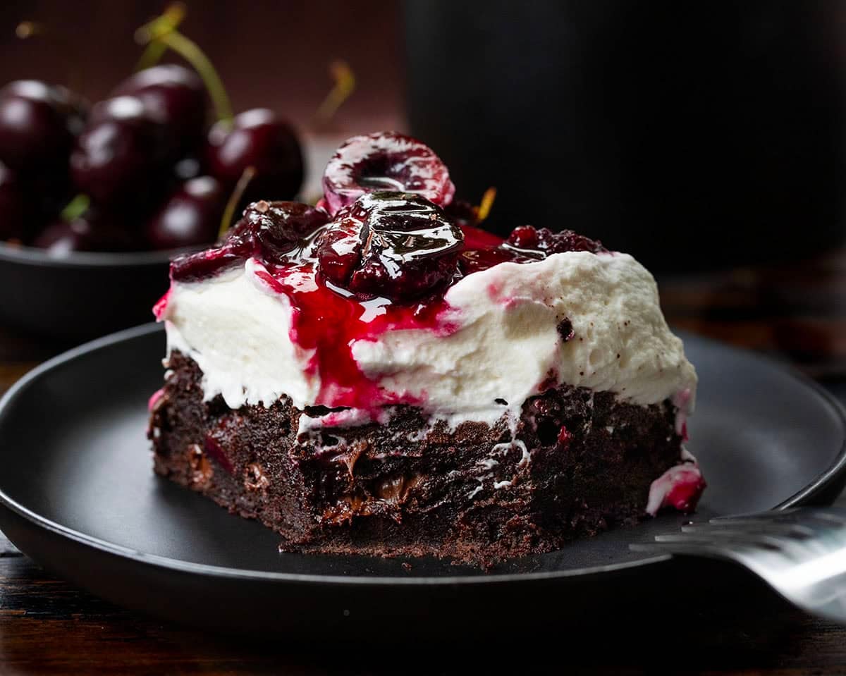 Close up of a Black Forest Brownie with a bite removed on a plate on a wooden table.