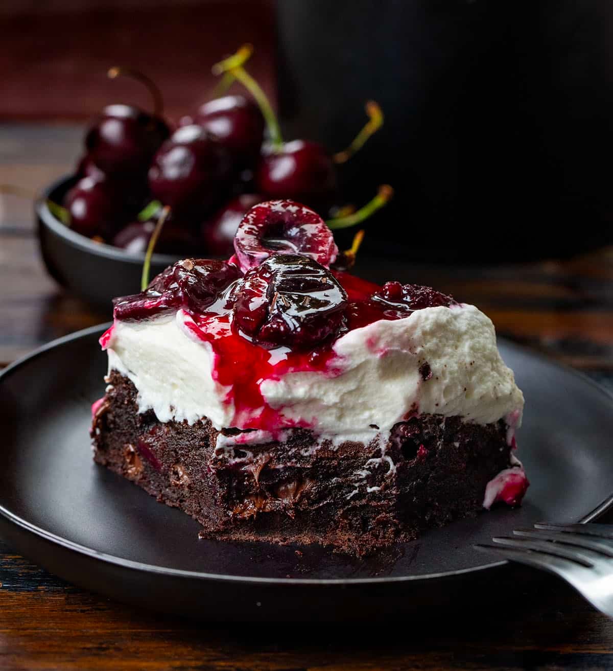 Black plate with Black Forest Brownie on it with a bite removed and the fork resting on the plate.