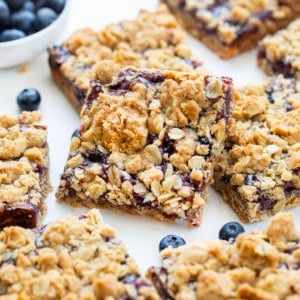 Close up of cut up Blueberry Oatmeal Crumble Bars on a white table with fresh blueberries.