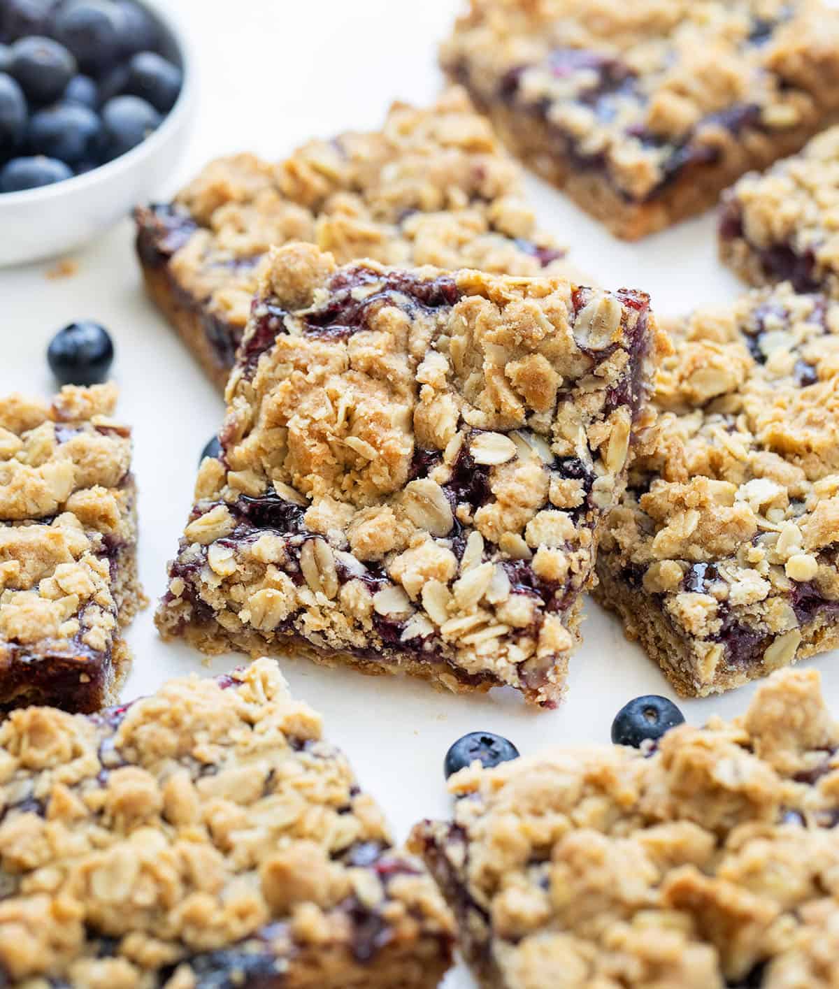 Close up of cut up Blueberry Oatmeal Crumble Bars on a white table with fresh blueberries.
