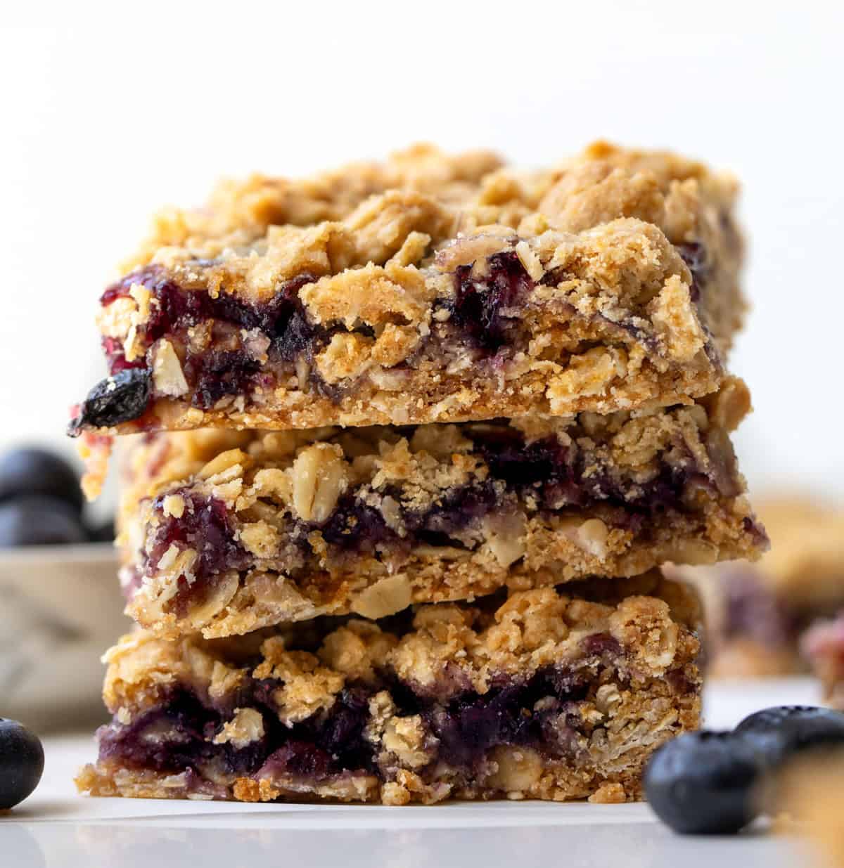 Stack of Blueberry Oatmeal Crumble Bars on a white table surrounded by more bars. Stack of Blueberry Oatmeal Crumble Bars on a white table surrounded by more bars.