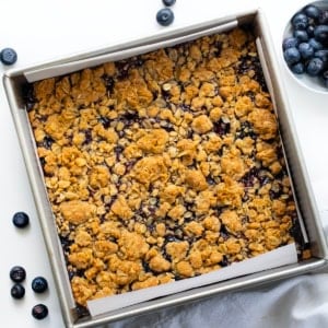 Pan of Blueberry Oatmeal Crumble Bars on a white table with fresh blueberries from overhead.