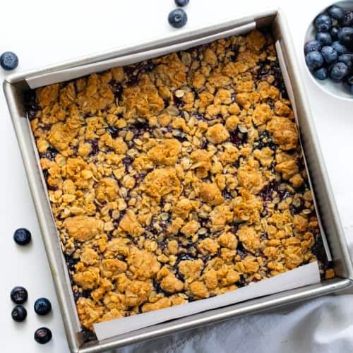 Pan of Blueberry Oatmeal Crumble Bars on a white table with fresh blueberries from overhead.