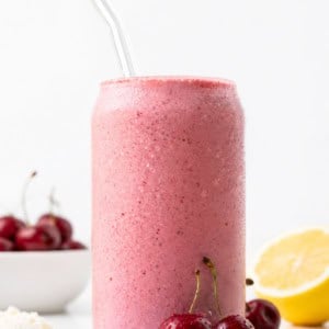Glass of Cherry Frosted Lemonade on a white table with cherries, ice cream, and lemon.